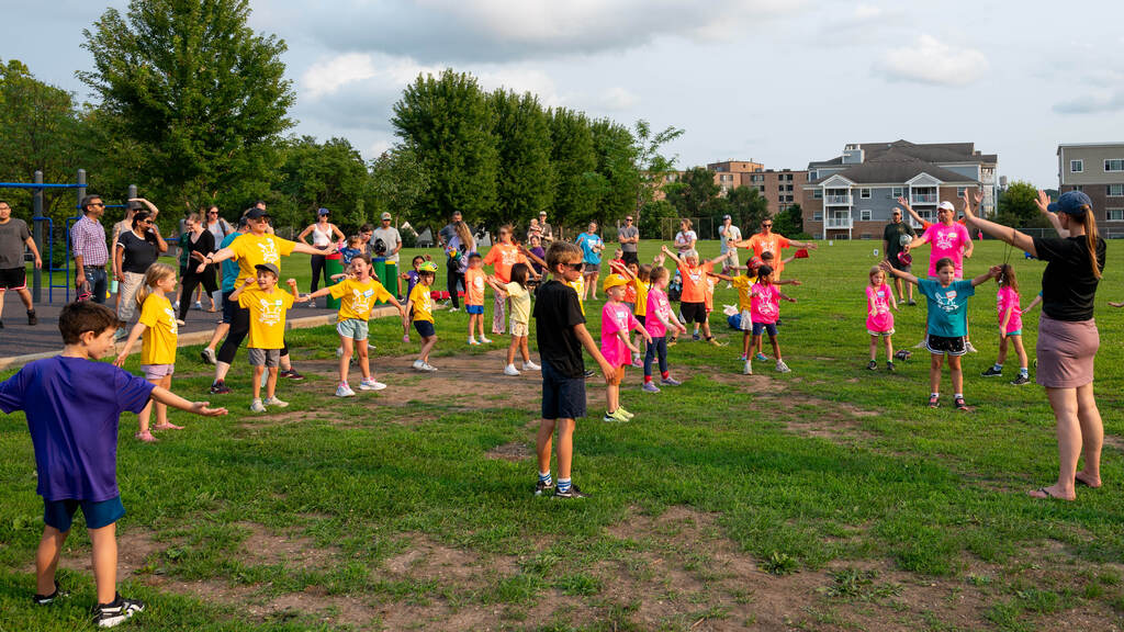 In a field. dozens of kids in bright shirts stretch before their tball practice.