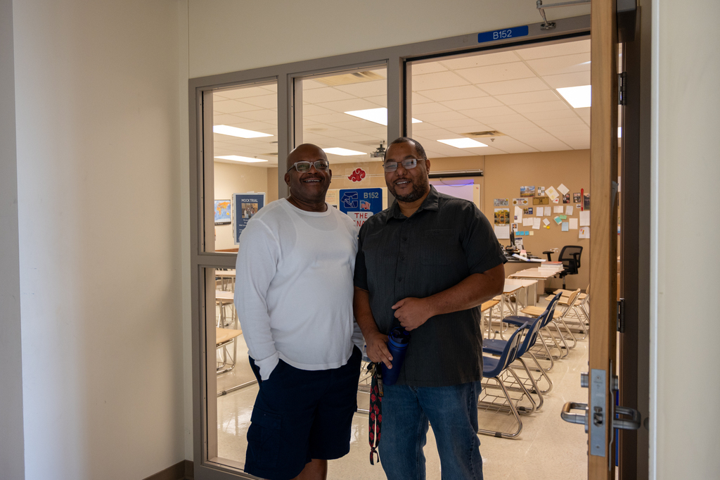 Two Century students waiting outside the classroom door to welcome students and smiling for a photo.