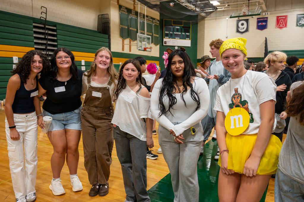 A group of students with nametags and costumes getting ninth grade students excited for the school year.
