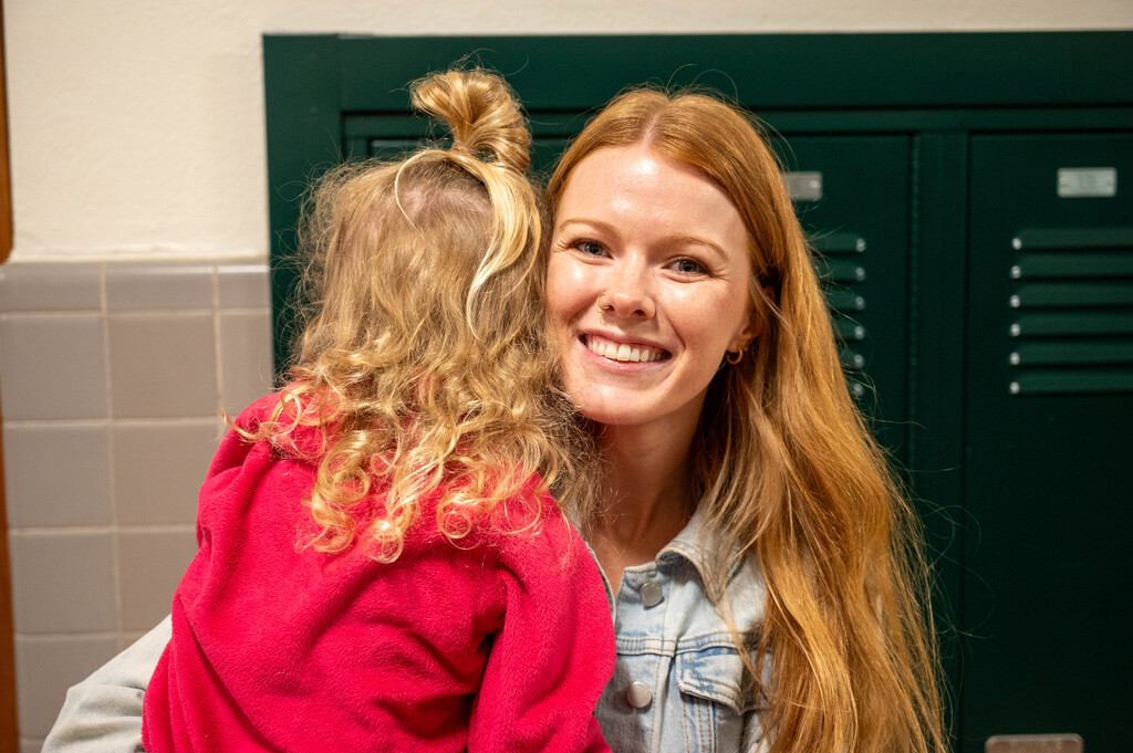 Parent embracing student for a hug while smiling at the camera in front of the lockers.