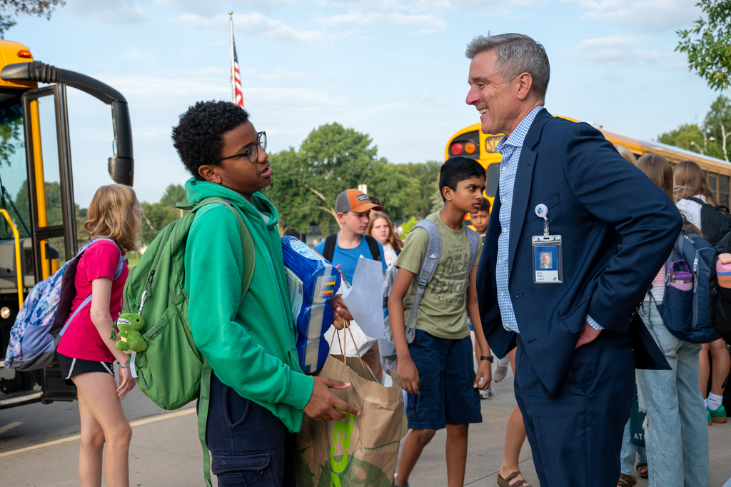 Superintendent Pekel talking with a student and laughing in front of the bus drop off zone