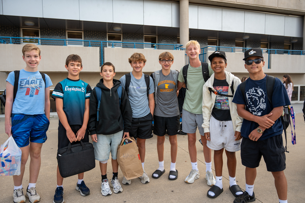 A large group of Kellogg students standing next to eachother smiling or posing for a photo in front of the Kellogg building.
