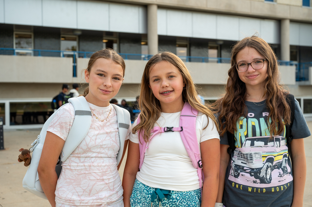 Three students standing together smiling for a photo with their backpacks on.
