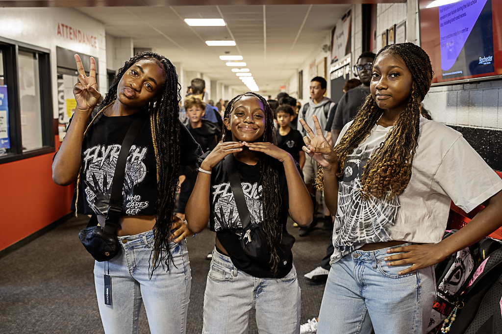 Three JA students posing for a photo as a group of 3 wearing matching shirts in the hallway.