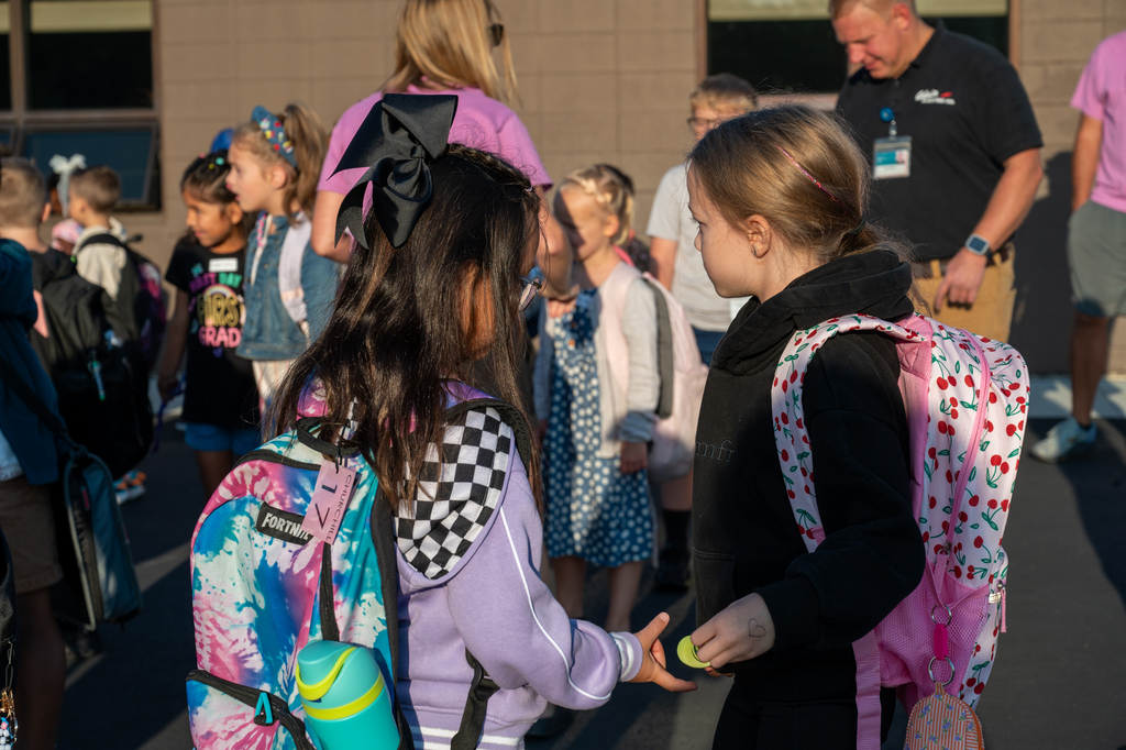 Two bestfriends reunited and sharing a toy in their hands with their backpacks to the camera.