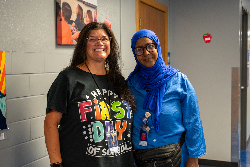 Two washington staff standing together next to a wall smiling for a first day of school photo.