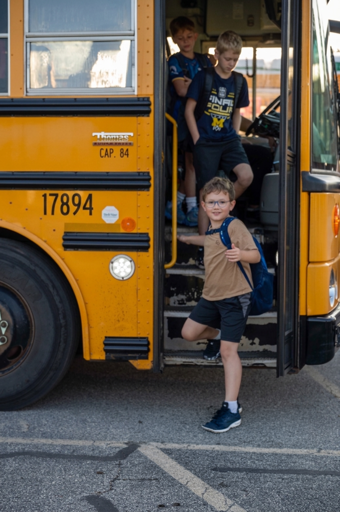 Student giving a thumbs up to the camera as they get off the bus.