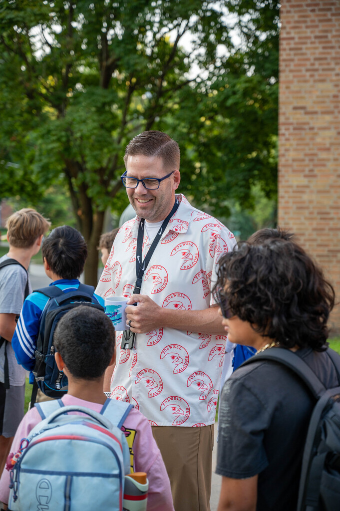 Teacher holding a coffee mug and smiling down as he talks with a student.