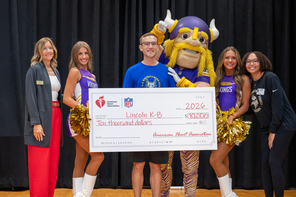 Wyatt Boberg holding a $10,000 donation check with Vikings cheerleaders, Viktor, and AHA Members.