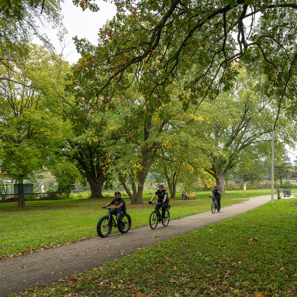 In a lush green park, three cyclists ride by.