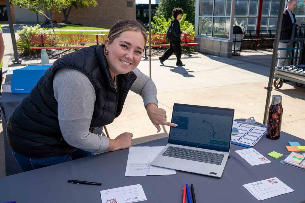 A volunteer smiles at the camera and points to the map on her laptop.