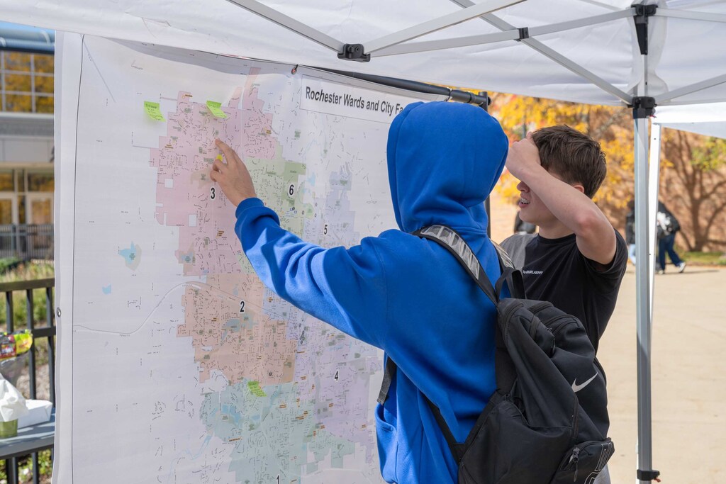A student in a hoodie points at a map of Rochester.