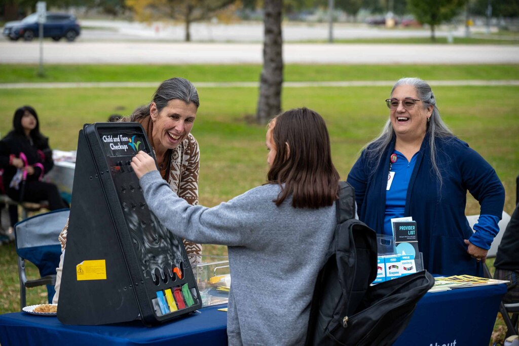 A teen plays a game at a resource table. The presenters smile.
