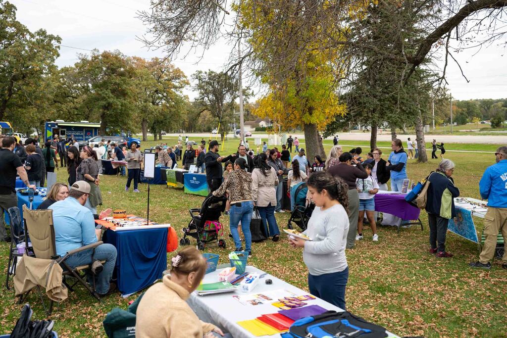 People visit tables of family resources lined up in a park.