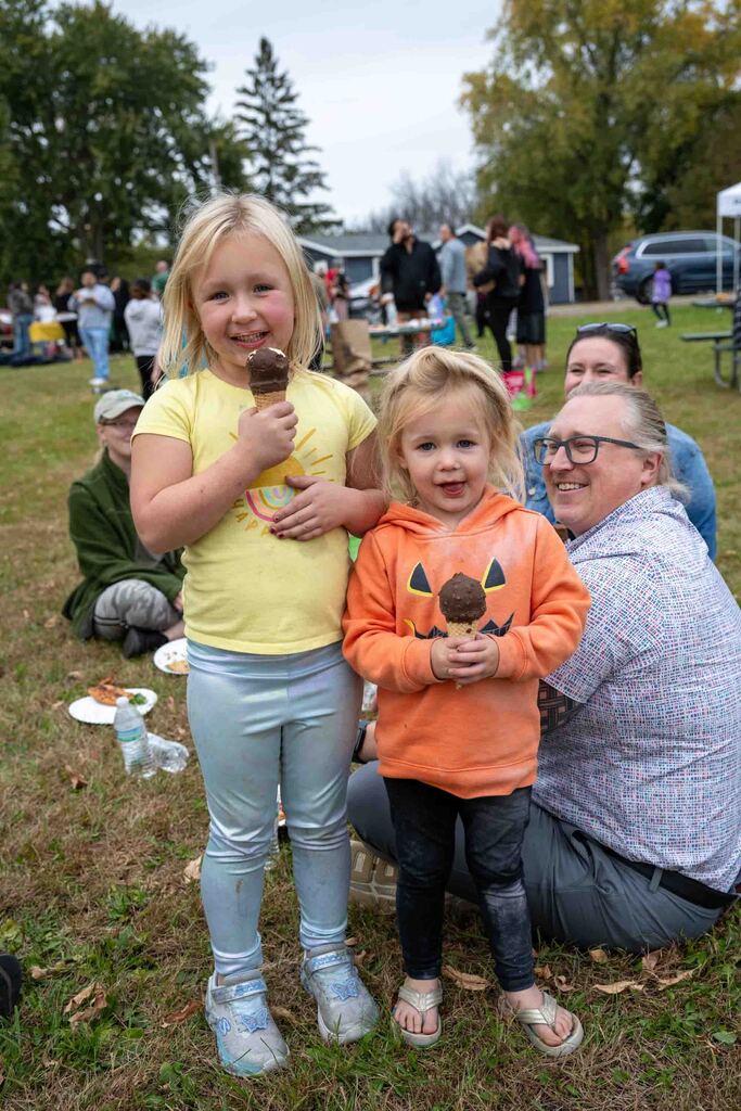 Two young sisters eat ice cream cones at the park.