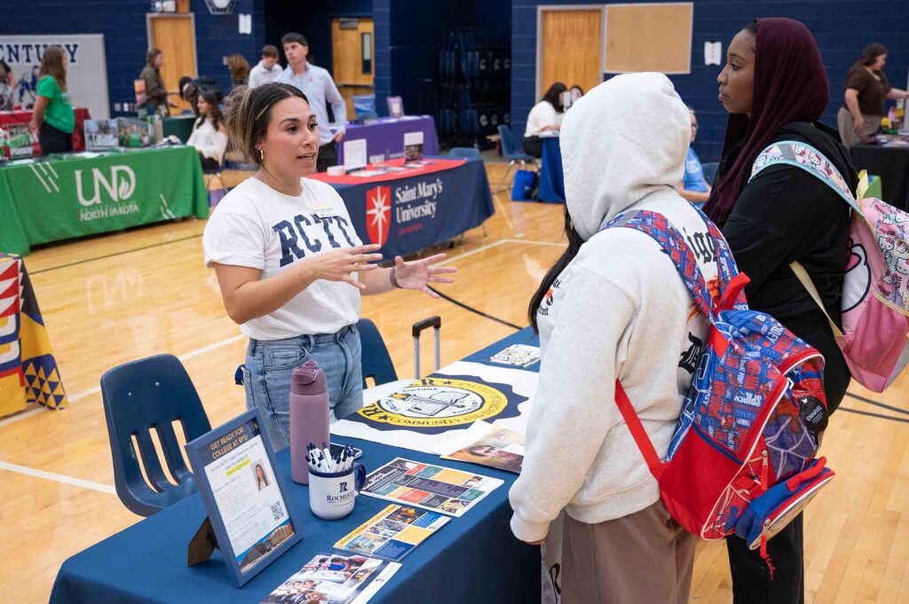 A woman presents a college option for two students at a table.