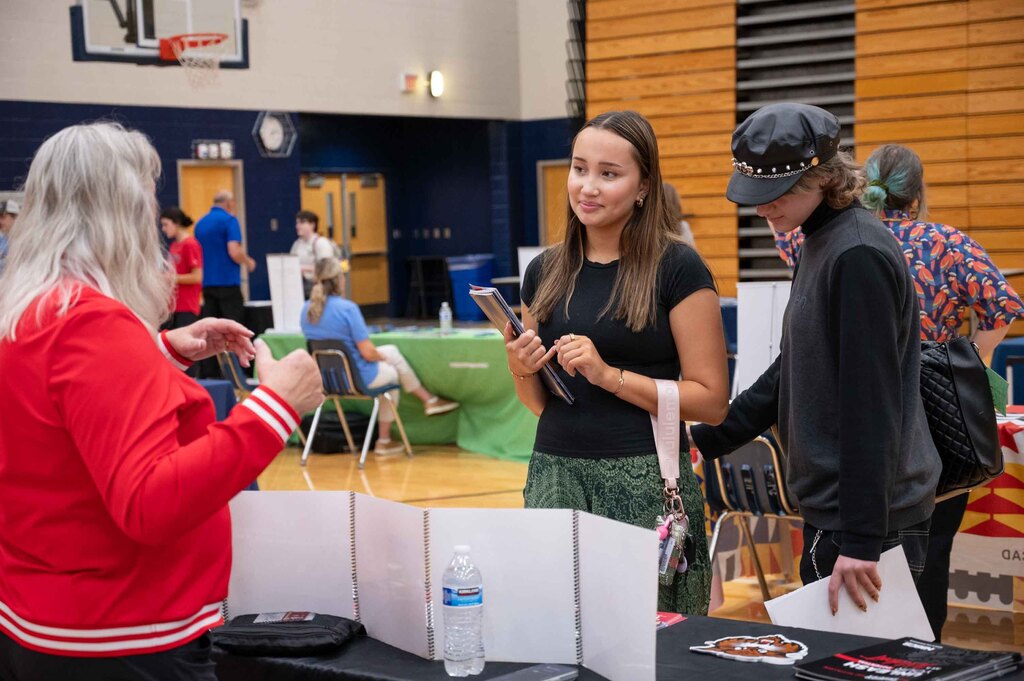 A woman presents a college option for two students at a table.