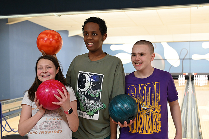 Three students smiling at the camera holding bowling balls