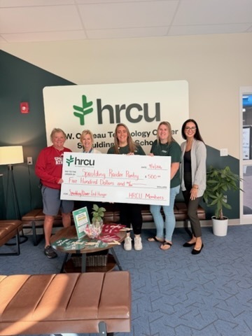 Five women hold a large check in front of a sign that reads "hrcu". One wears a red shirt.