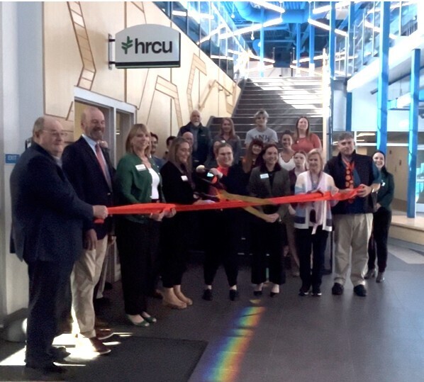A group of people holding a red ribbon for a ribbon-cutting event at an hrcu facility.