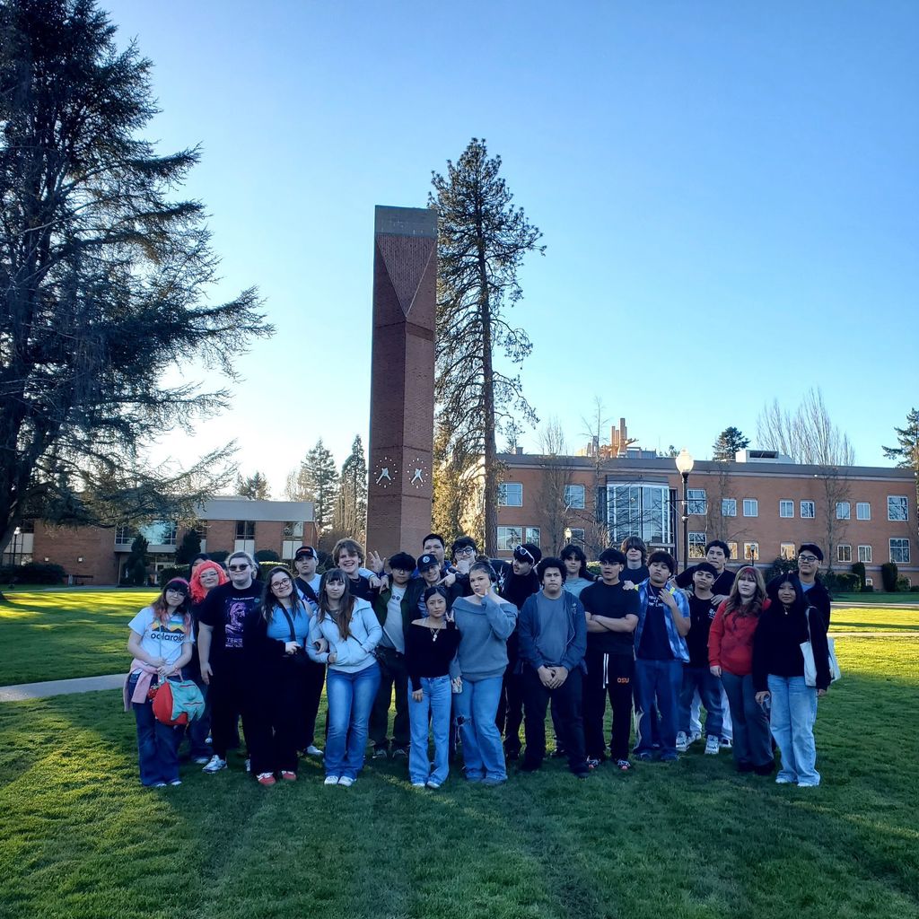 A group of students poses in front of a tall structure on a grassy lawn.