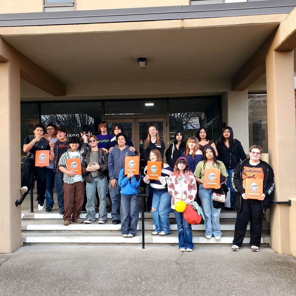 Group of students standing on steps in front of a building, holding orange posters.