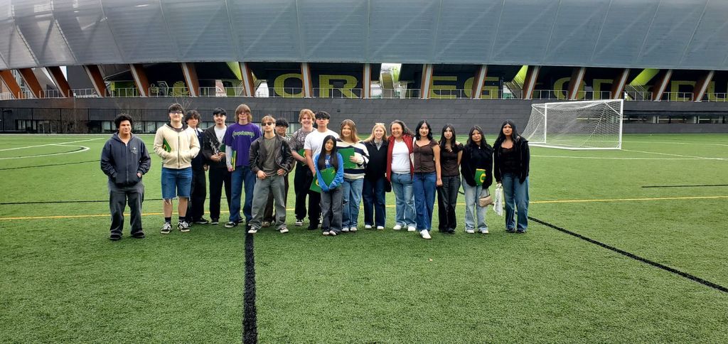 A group of people standing in a line on a soccer field, stadium in the background.