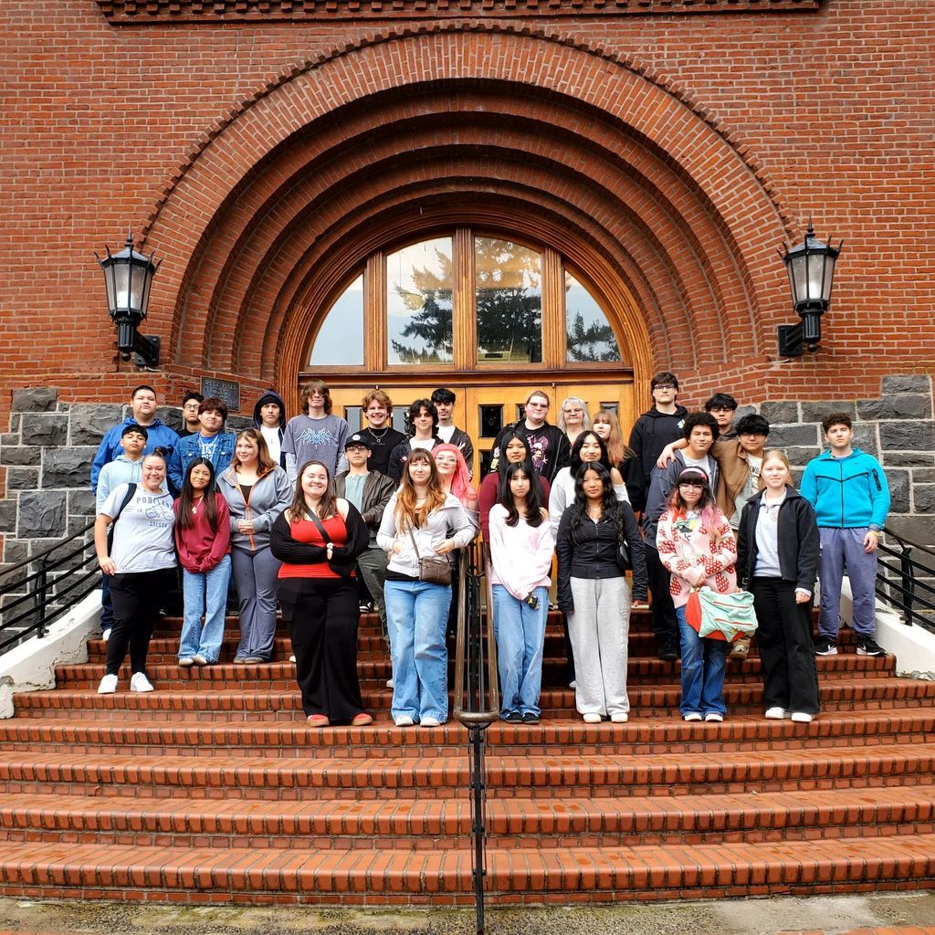 A group of people stands on stairs in front of a brick building with an arched entrance.