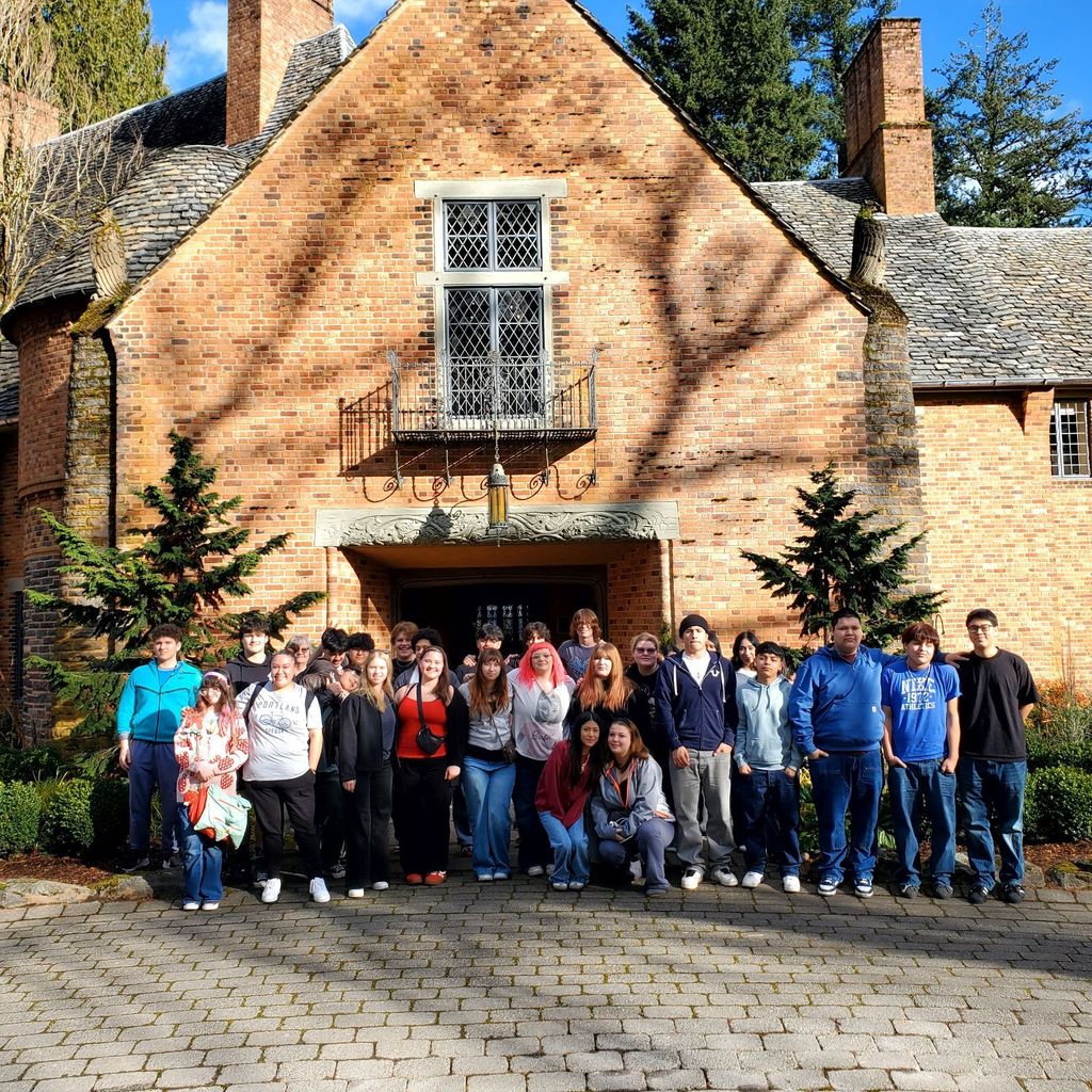 A group of people stands outside a brick building with a balcony and windows.