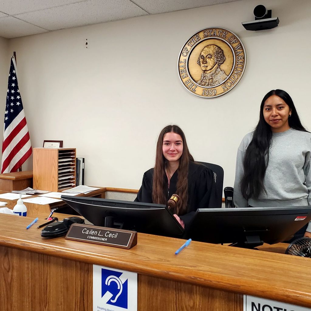 Two women seated at a desk with computer monitors. One has long hair and the other has short hair.