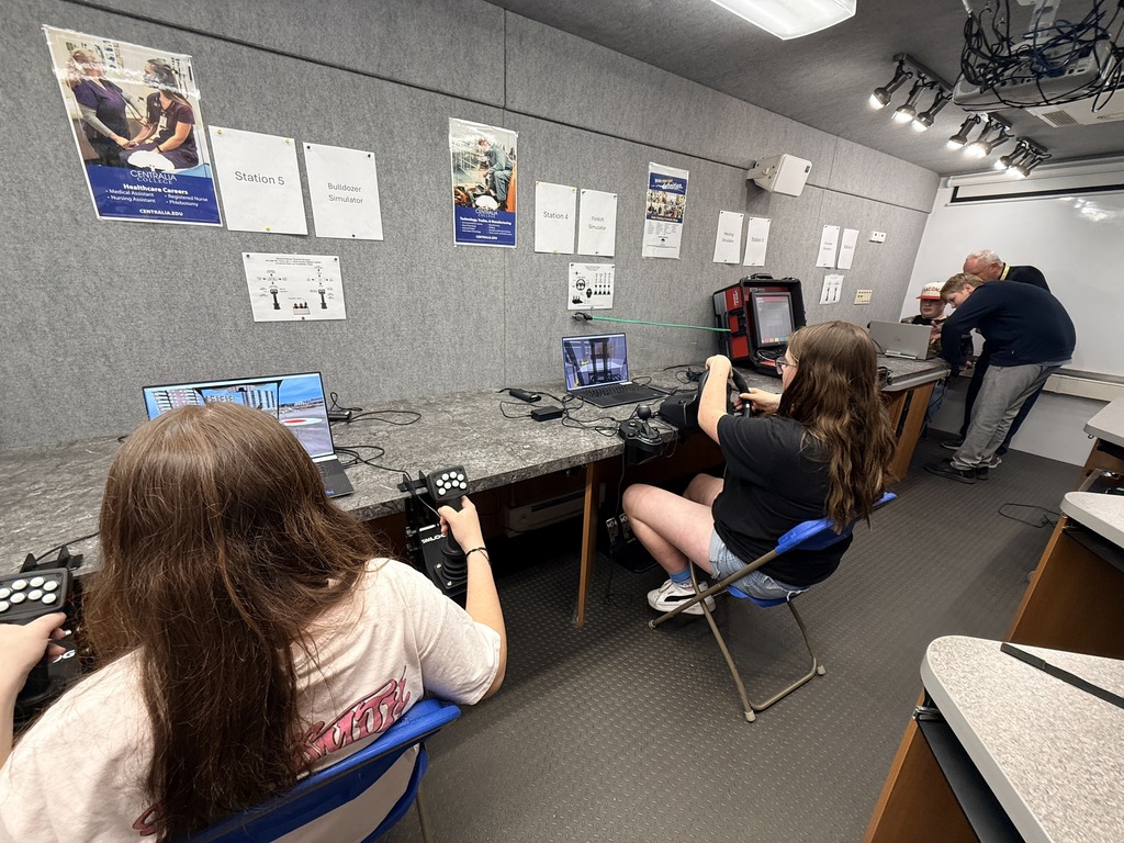 Two people seated at a desk with laptops, working in a room with posters on the wall.