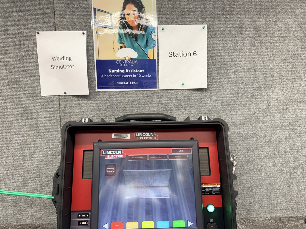 A red and black device with a screen displaying a blue background. Two posters are above the device.