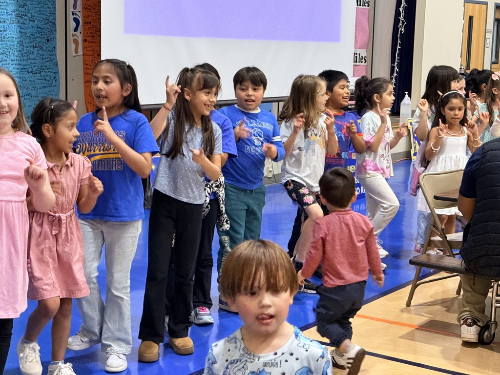 A classroom with children in various colored clothing, lined up for a dance or activity.