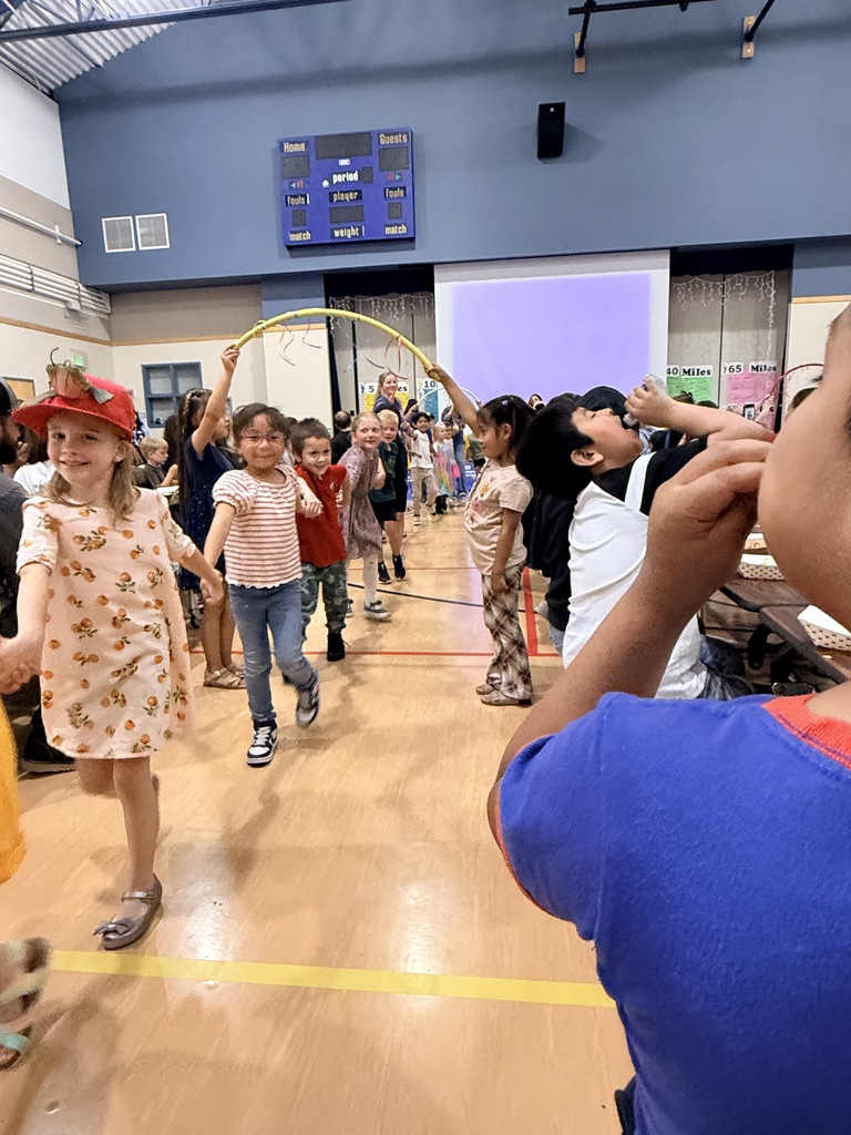 A group of children in a gymnasium, some holding a hula hoop, while others watch or participate.
