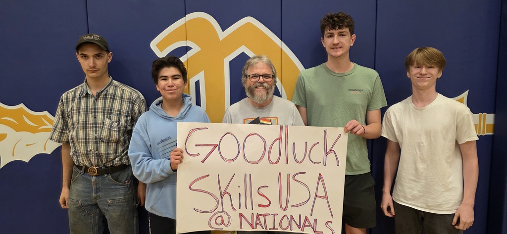 Five individuals stand together with a sign reading "Good luck SkillsUSA @ NATIONALS" in front of a blue backdrop.