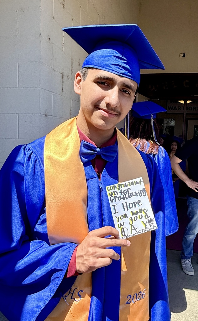 A male in a blue graduation gown holds a handwritten card that reads, "I hope you have a good day."