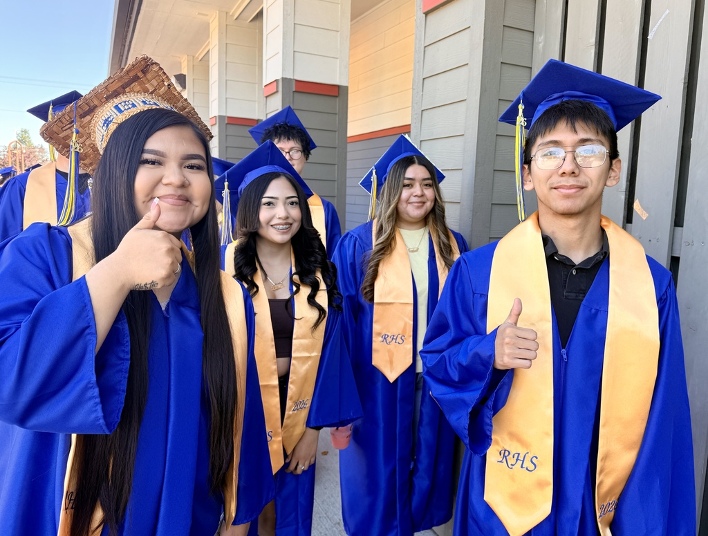 A group of students in blue graduation gowns and caps, smiling and posing for a picture.