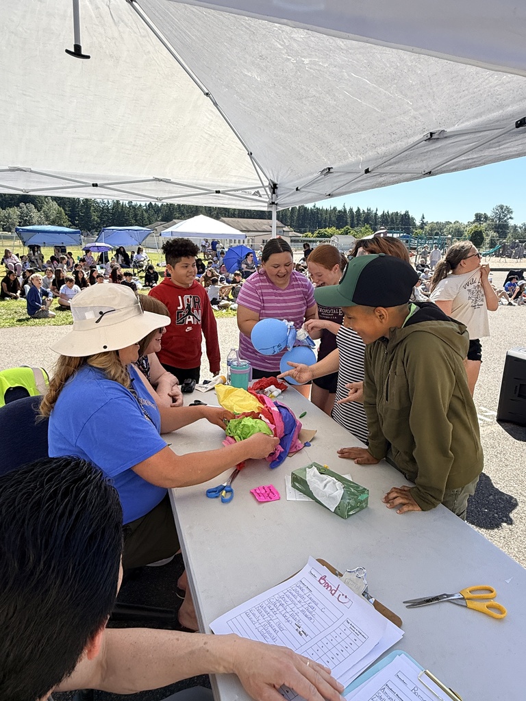 People under a canopy. A woman in a blue shirt helps a boy with a hat on.