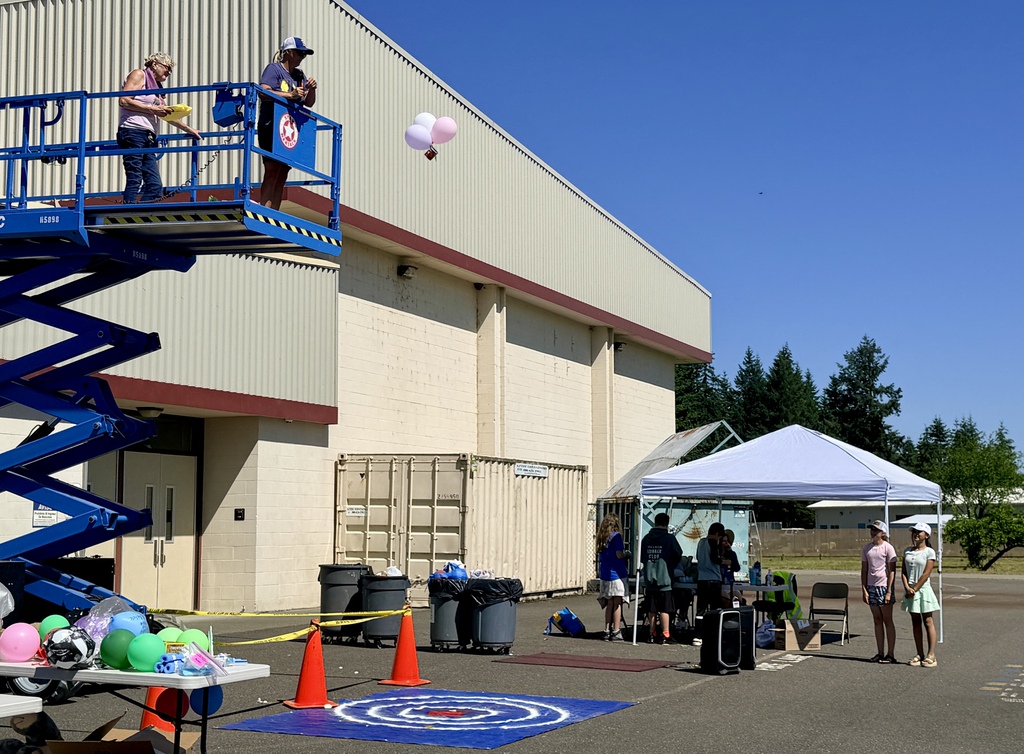 A group of people stand outside a building with a blue lift. One person stands on the lift.