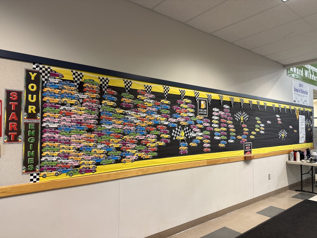 A bulletin board displays colorful race car images on a black background with "Your Start" above. A table with items stands nearby.