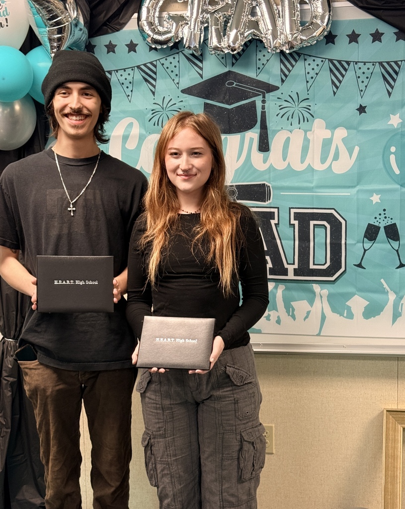 A young man and woman pose with diplomas. They stand under a "Congratulations Grad" banner.