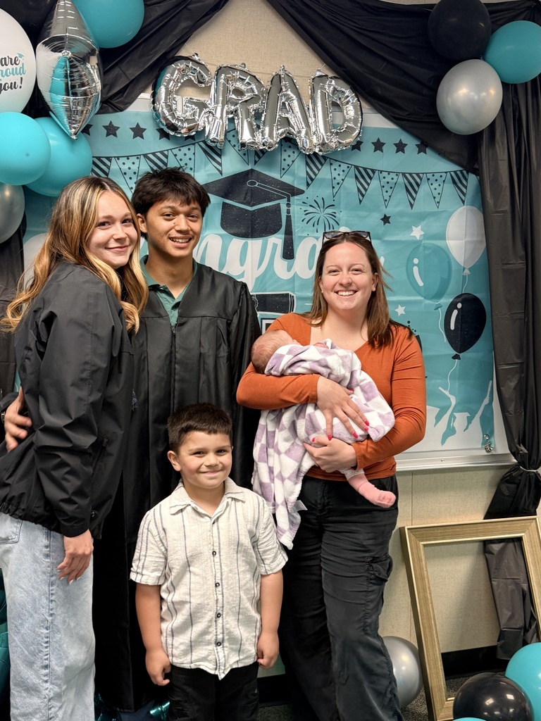 Family members in a room with balloons and a banner that says "Grad" standing together with a baby.