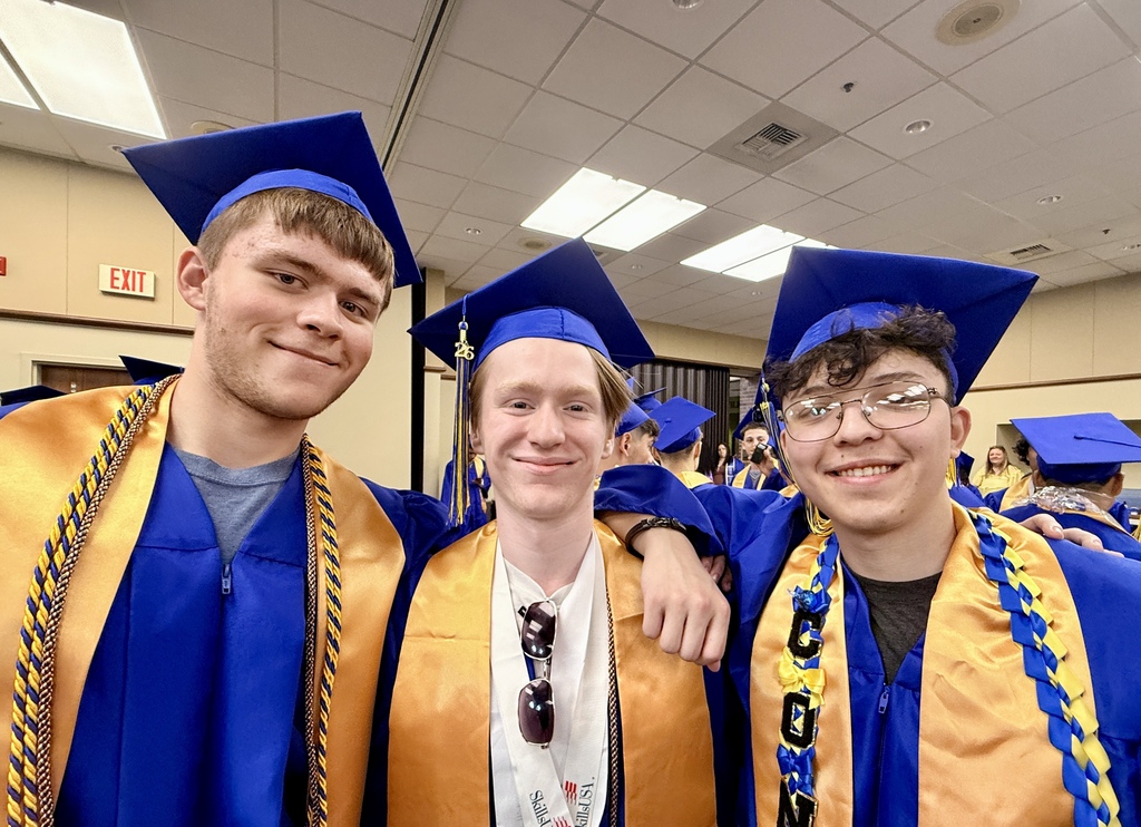 Three young men in graduation caps and gowns, two wearing blue and gold, smile and pose for a picture.