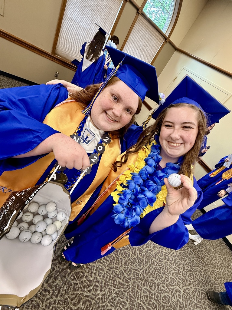 Two women in blue and yellow graduation gowns and caps. One holds a golf bag, and the other holds a golf ball.