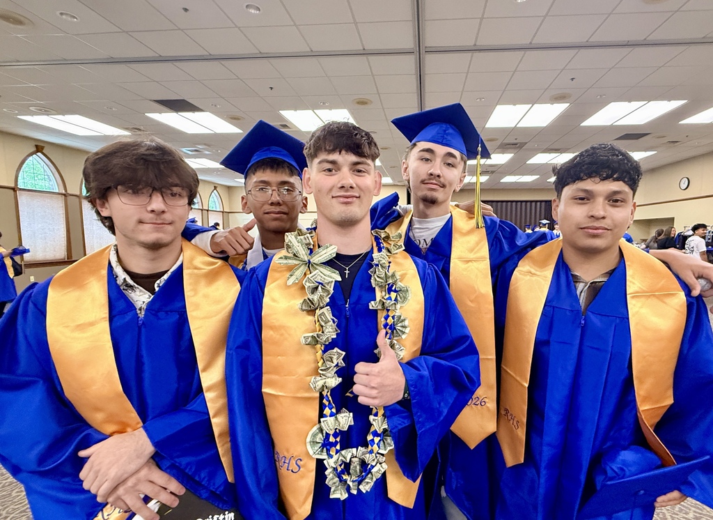Five men in blue and gold graduation gowns and caps pose for a photo in a room.