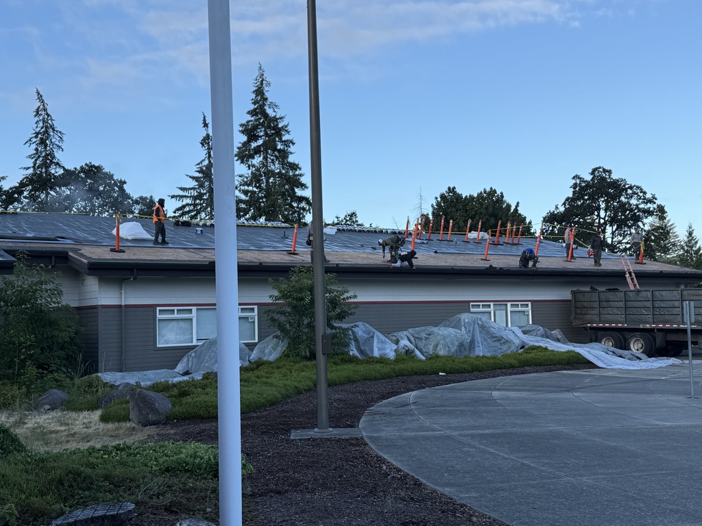 Construction workers on the roof of a building. A road, pole, and trees surround the building.