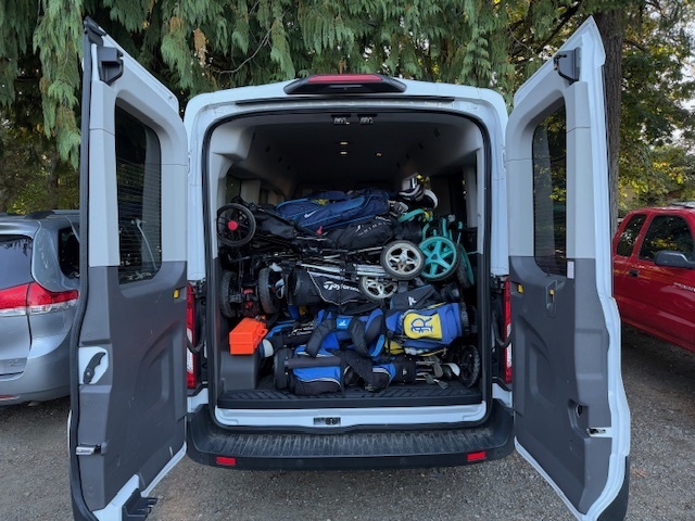 Rear of a van with its doors open, showing a loaded cargo area with various sports equipment and bags.