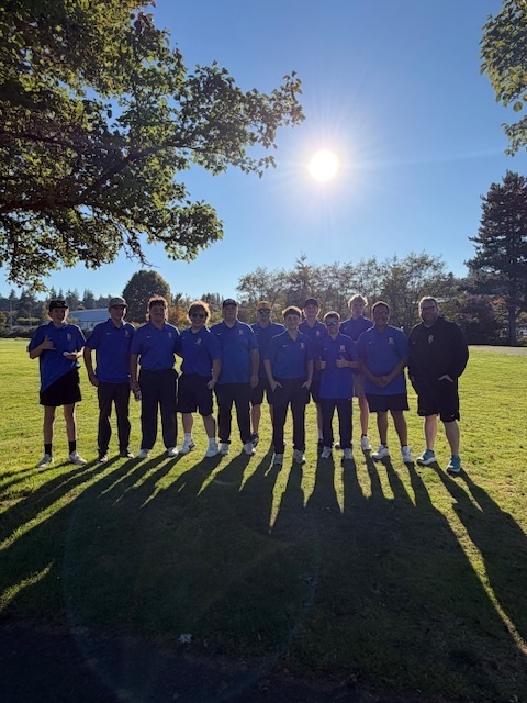 Eleven people in blue shirts and black shorts stand in a line on a grassy field.
