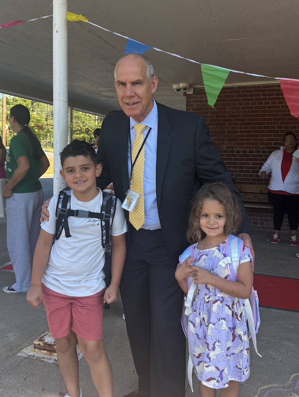 Superintendent posing with two students at kdm front door
