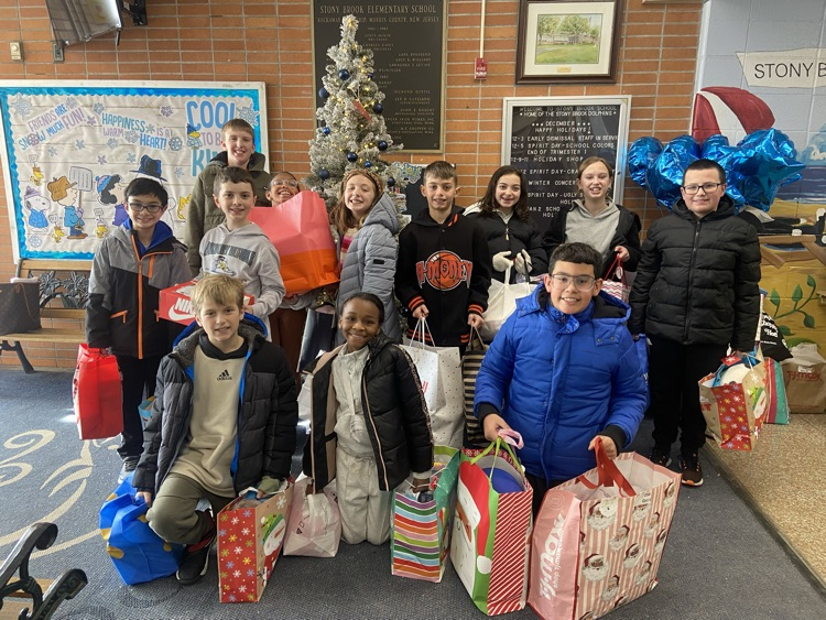 .Female and Male 4th grade students with presents on hand  while posing in front of the school's giving tree . 